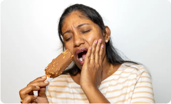 A woman wincing with tooth sensitivity while eating an ice-cream bar
