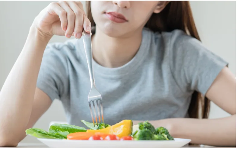 A woman with little appetite pushing salad around her plate